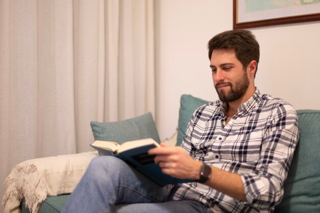 A man sits on a couch reading a book.