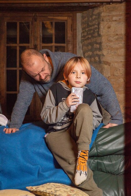 A man sits on a couch with a boy wearing orange shoes that say's " on the side.