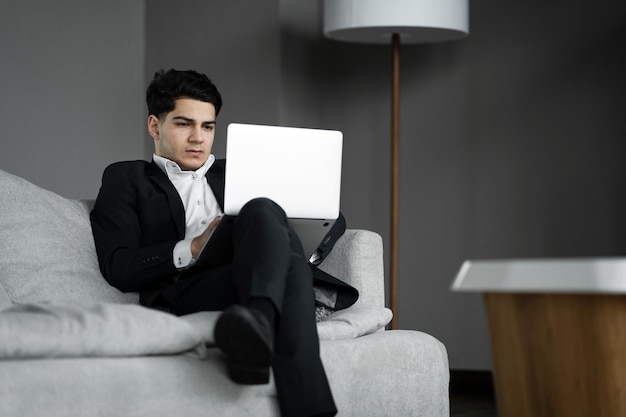 A man sits on a couch with a laptop in his lap.