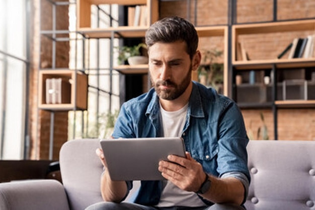 a man sits on a couch with a tablet in his hands