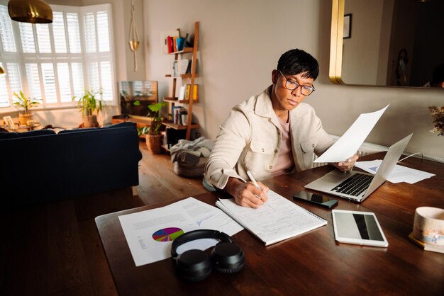 A man sits at a desk in front of a laptop and a pair of headphones.