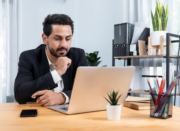 A man sits at a desk in front of a laptop.