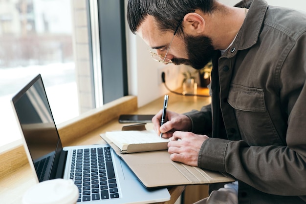 A man sits at a desk with a laptop and a cup of coffee on the table.