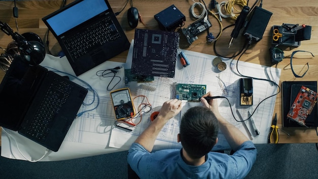 A man sits at a desk with a laptop, a laptop, a laptop, and a circuit board.