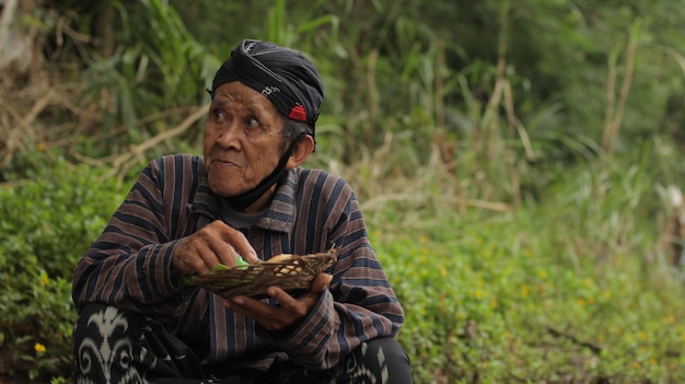 Photo a man sits in a field with a basket of bamboo.