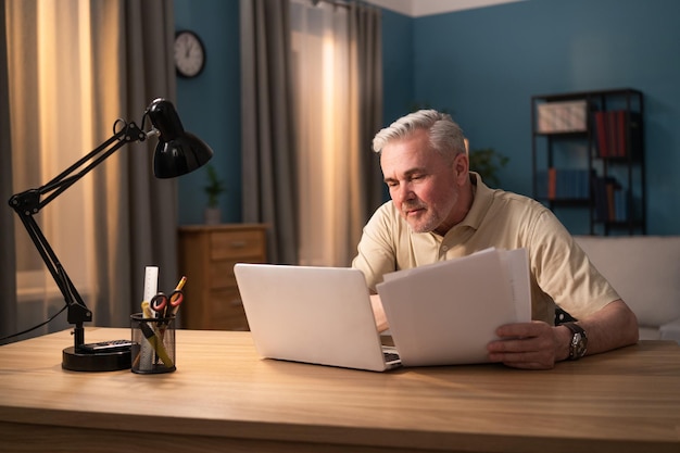 A man sits in front of a computer in his living room in the evening an elderly man sits at a laptop