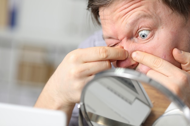 Man sits in front mirror and crushes his face