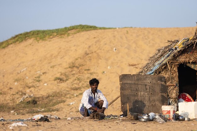 A man sits in front of a shack on the beach.