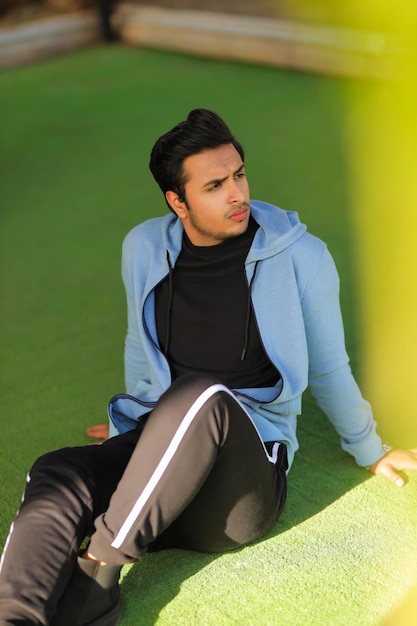 A man sits on a green field, wearing a blue hoodie and black pants.