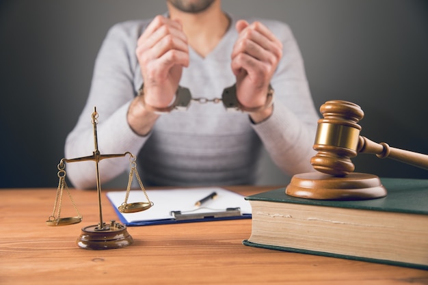 a man sits in handcuffs by a hammer and scales