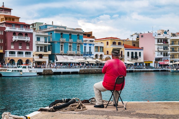 A man sits in the harbor with a fishing rod in front of colorful buildings