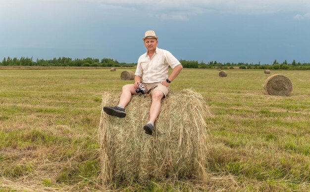 A man sits on a hay bale in a field