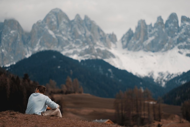 男は山々を背景に、山の前の丘に座っています。