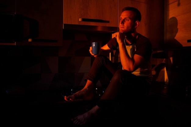 A man sits in the kitchen in the sunset light and drinks coffee