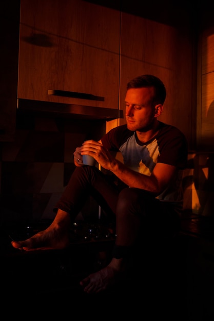 男は夕日の光の中でキッチンに座ってコーヒーを飲みます