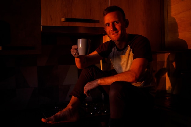 Мужчина сидит на кухне в лучах заката и пьет кофе