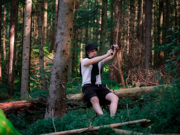 A man sits on a log and takes pictures in the forest