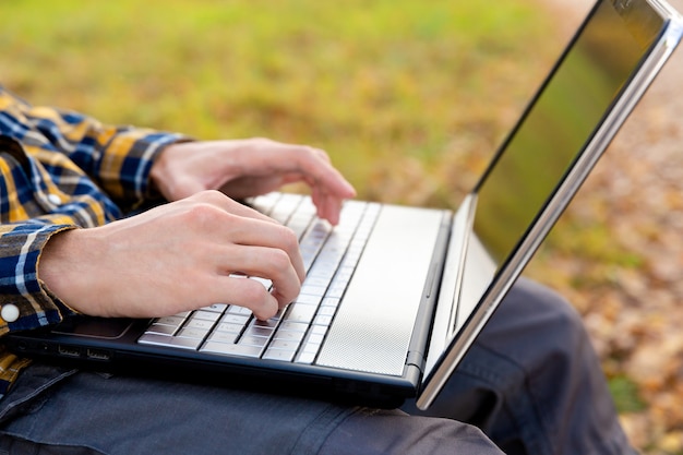 Man sits in park and works at laptop outdoors Hands typing on keyboard