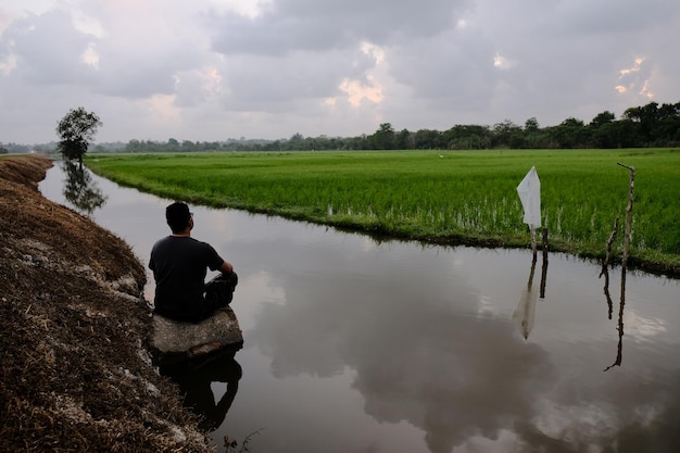 A man sits on a river bank in front of a sign that says'no water '