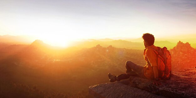 A man sits on a rock looking at the sunset