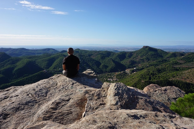 A man sits on a rock overlooking a valley.