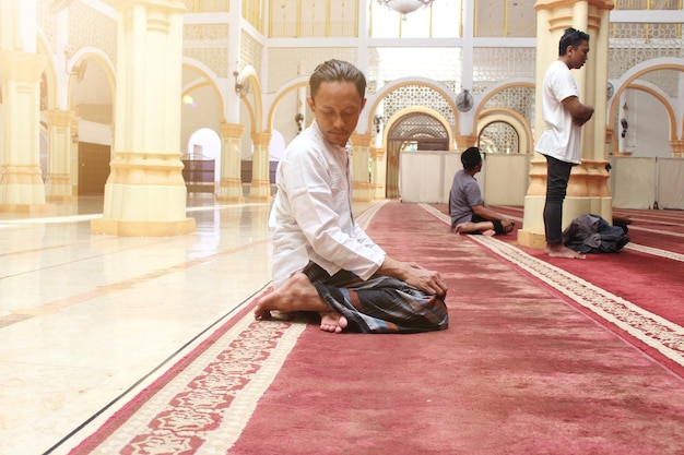 A man sits on a rug in a mosque with other people.