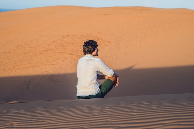 A man sits on the sand in the desert.