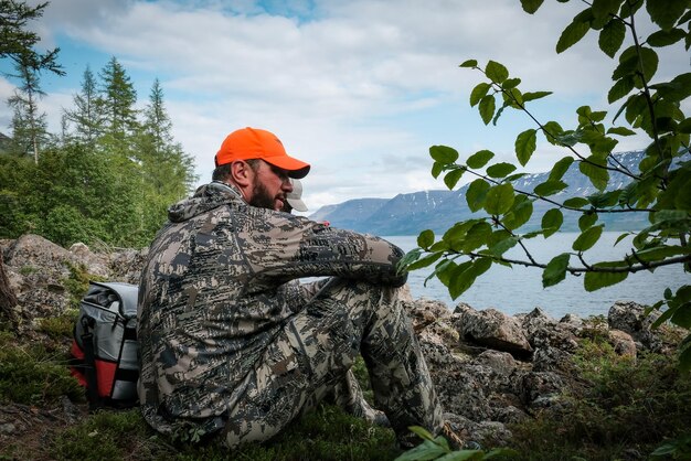 A man sits on the shore of a lake and looks out to the water.