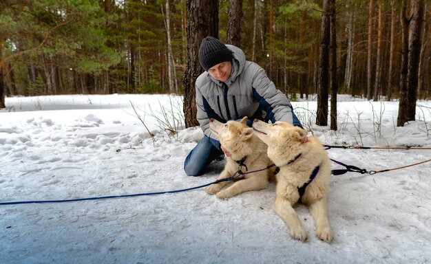 A man sits next to a sled of Siberian huskies.