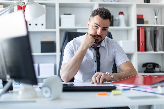 A man sits at a table in the office and looks at the wristwatch.