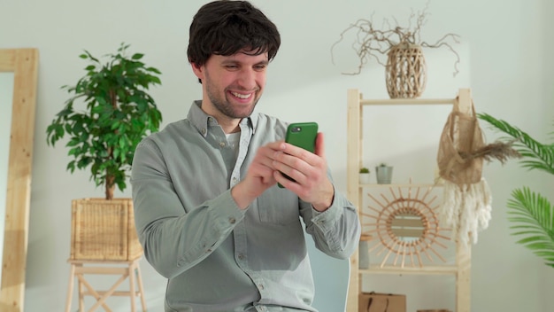 Man sits at a table, triumphantly wins an online lottery on a mobile phone, reads good unexpected news on a smartphone