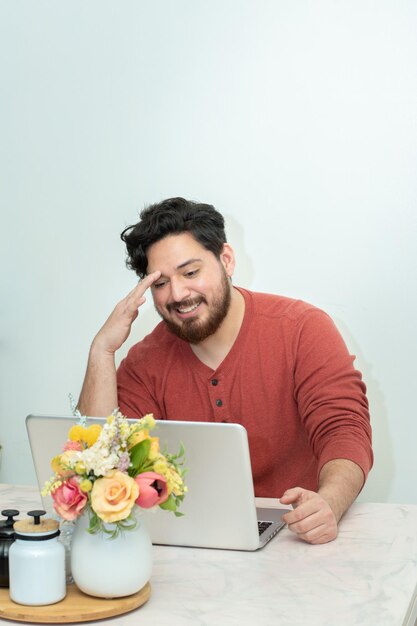 A man sits at a table with a laptop and a bouquet of flowers on it