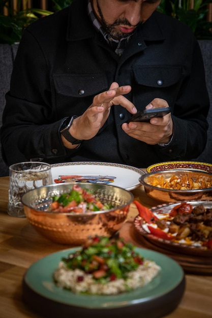 Foto un uomo siede a un tavolo con piatti di cibo e un piatto di cibo con un uomo che usa un telefono.