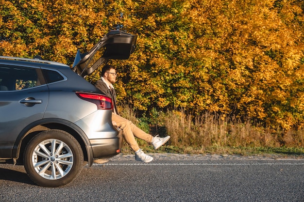 man sits in trunk of car and enjoys autumn sun