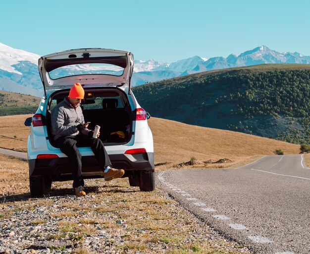 Man sits in the trunk of his car on the side of the road in the mountains