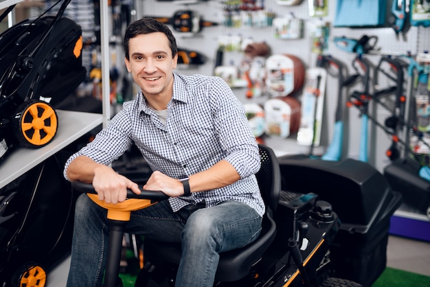 A man sits behind the wheel of a lawnmower and smiles.