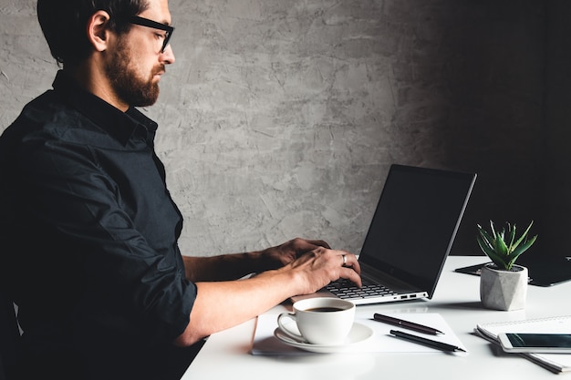 A man sits with a laptop in a black shirt. Business concept, work. Office routine. Property efforts