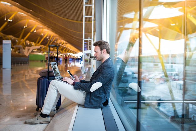 Equipaggi la seduta all'aeroporto facendo uso del computer portatile e del telefono cellulare accanto alla finestra