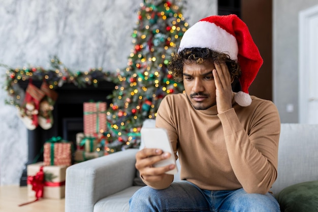 Man sitting alone on sofa for christmas at home hispanic received online notification on phone