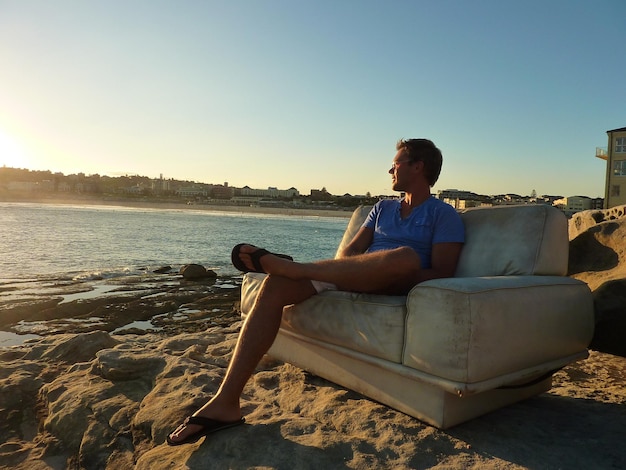 Photo man sitting on armchair at beach against sky