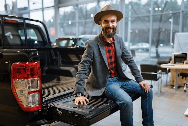 Man sitting in the back of new pickup truck in car dealership. Customer in vehicle showroom, male person buying transport, auto dealer business