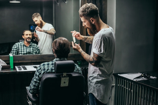 man sitting in the barber chair and smiling while a barber combing his hair