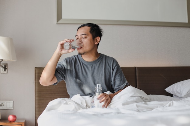 Man sitting on the bed and drinking a glass of mineral water after wake up from sleep