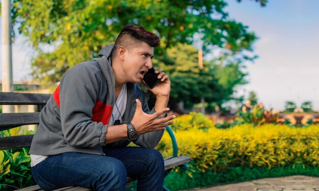 ベンチに座って電話をかけている男怒っている男が公園で電話をかけている