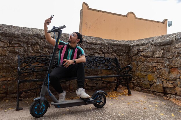 Man sitting on a bench taking a selfie with his electric scooter horizontal background  stone wall