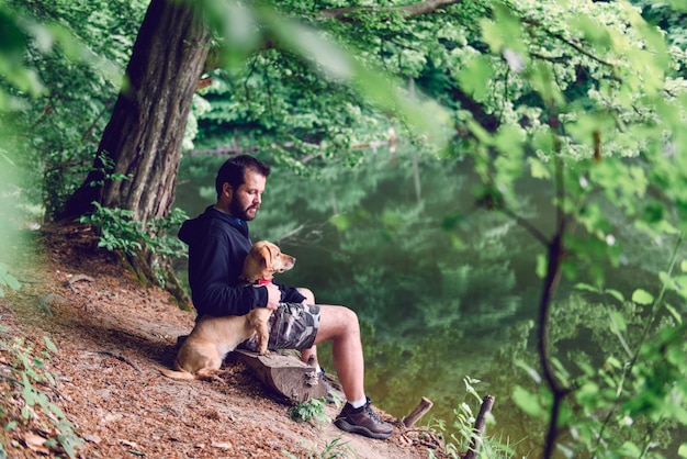 湖のほとりに犬と一緒にベンチに座っている男