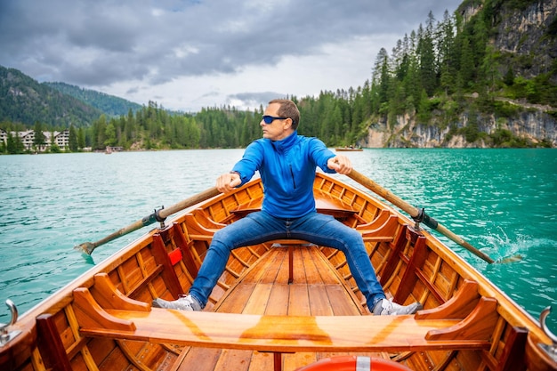 Photo man sitting in big brown boat at lago di braies lake in cloudy day italy summer vacation in europe