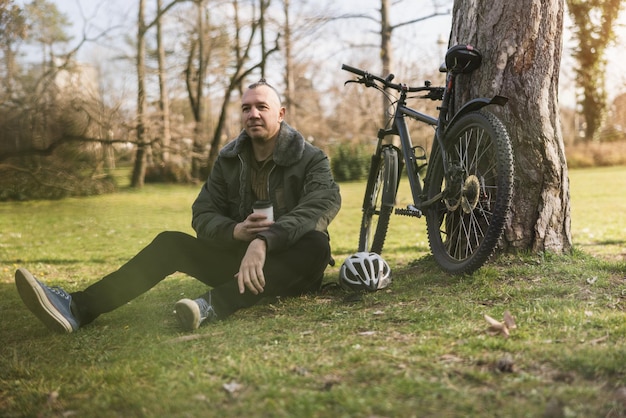 Man Sitting Next to Bike on a Meadowin a City Park