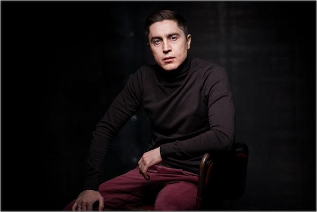 A man sitting on a brown leather chair on a black background. Card emotions. man emotions