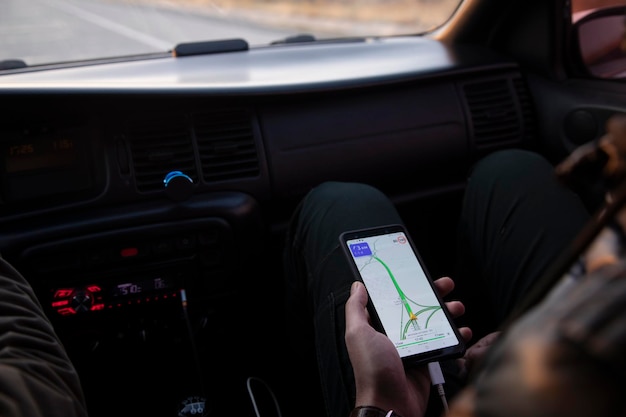 Мужчина сидит в машине и держит смартфон с приложением GPS-навигации по карте